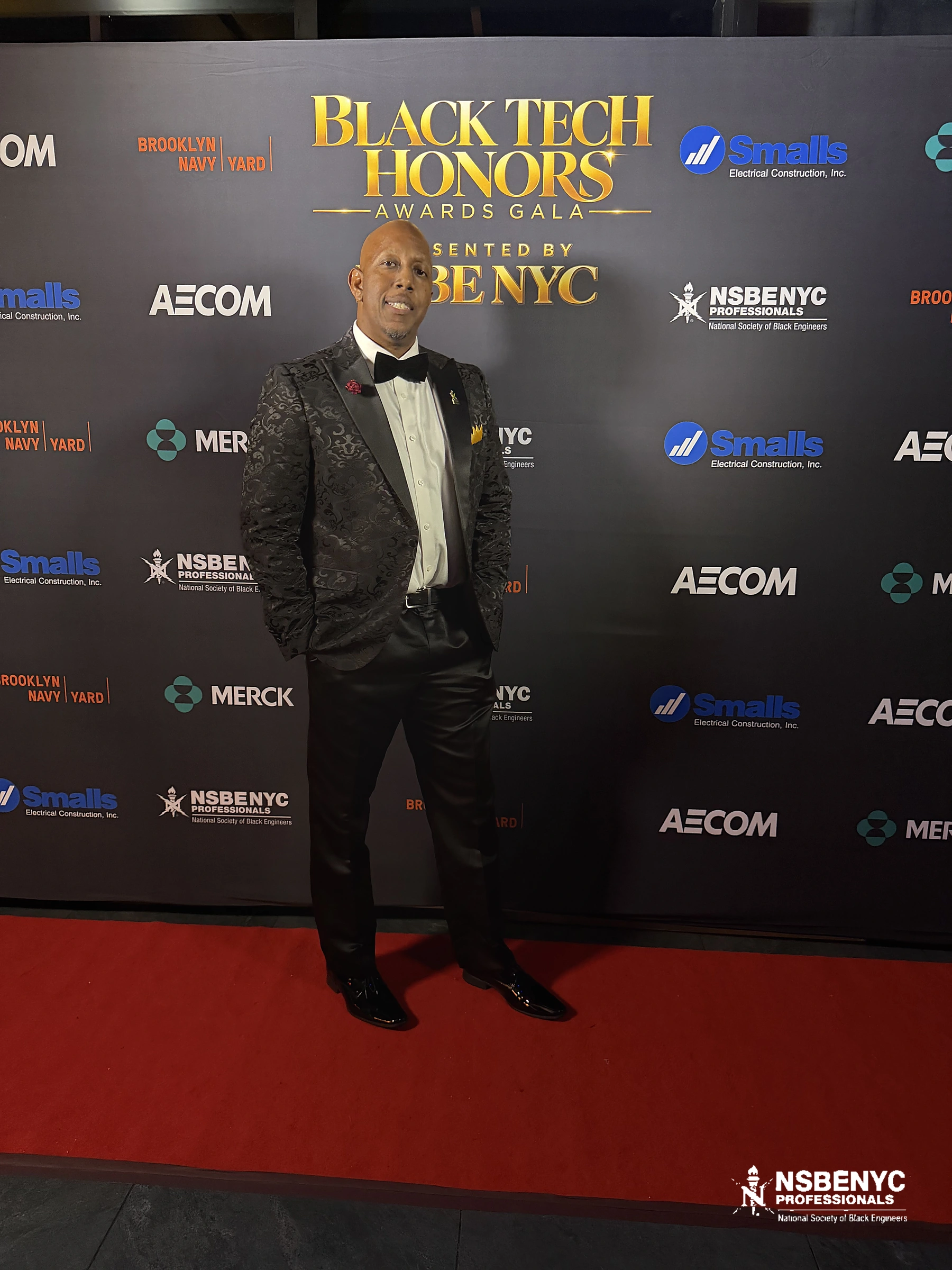 Gala guest in a patterned black tuxedo standing on the red carpet before the Black Tech Honors and partner backdrop